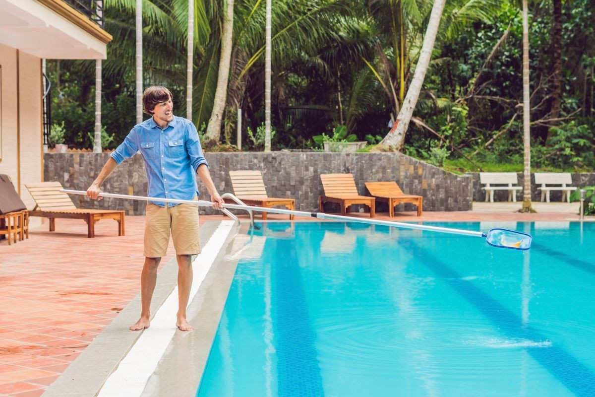 Cleaner of the swimming pool . Man in a blue shirt with cleaning equipment for swimming pools, sunny